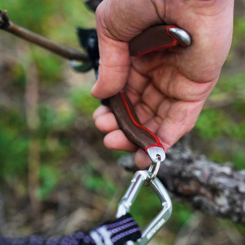 Hand securing a climbing carabiner to a harness with a leather grip for safety and comfort.